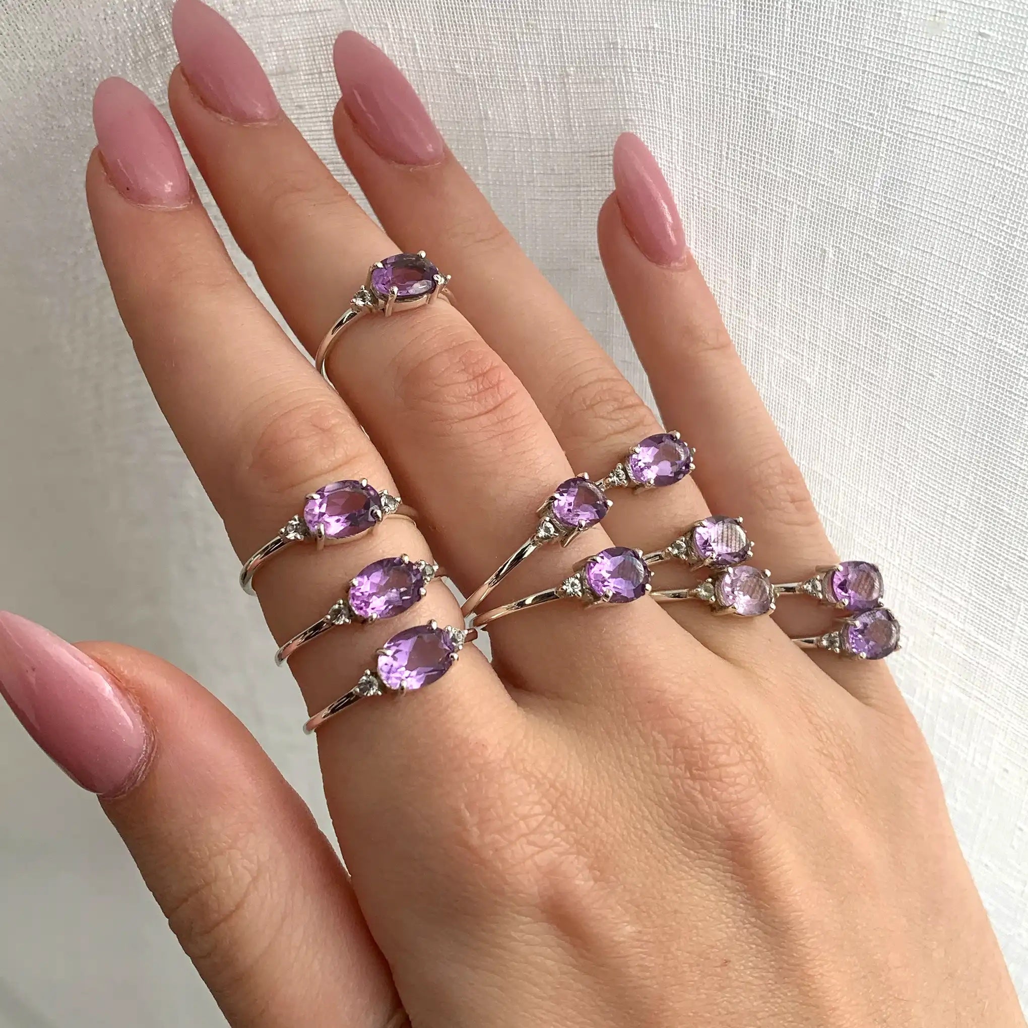 Hand wearing multiple sterling silver rings with natural pink amethyst gemstones 