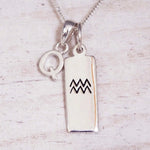 Sterling Silver Q Initial and Aquarius Necklace on a fine silver chain against a light wooden background