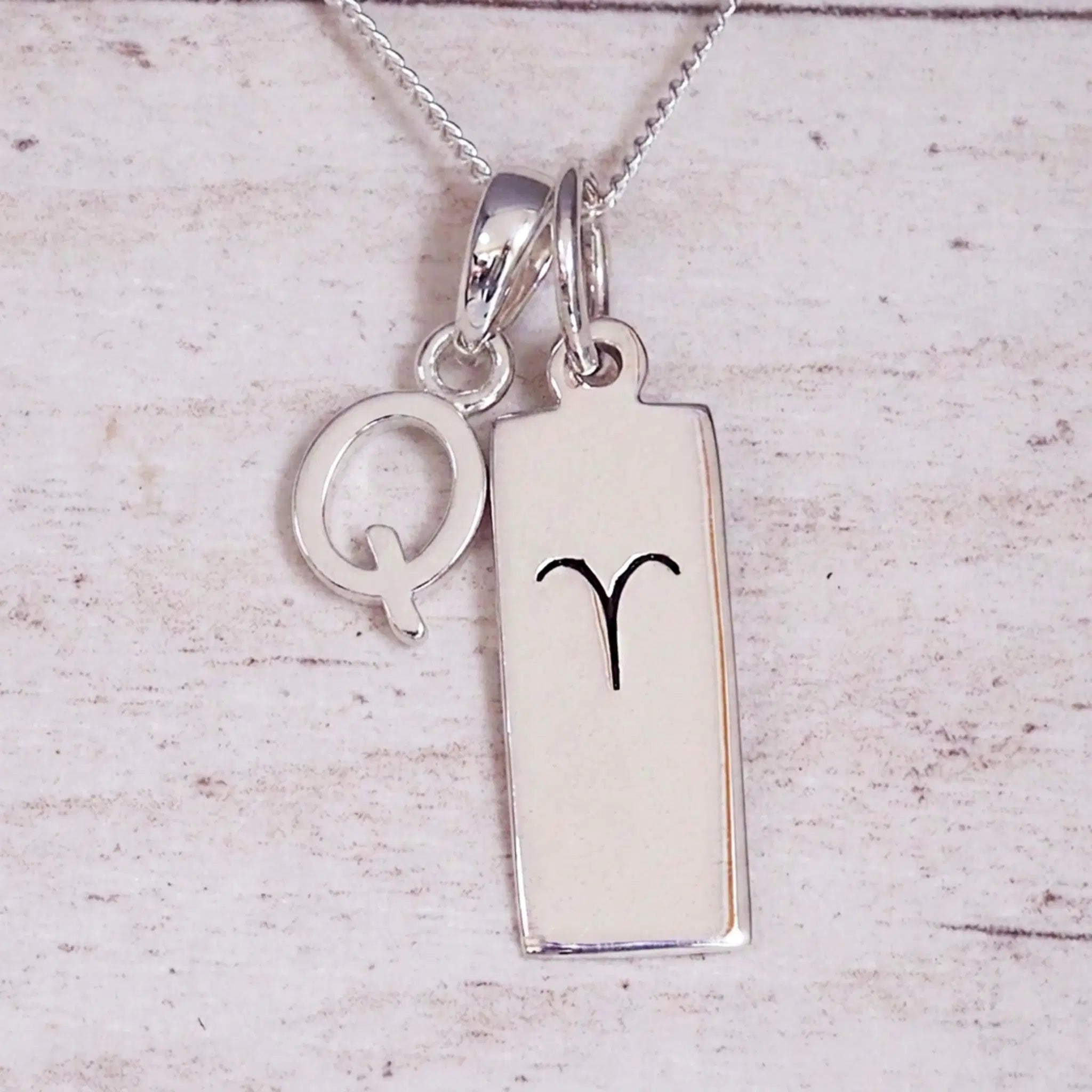 Sterling Silver Q Initial pendant and Aries necklace on a fine silver chain on a light wooden background