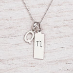 sterling silver initial Q pendant and capricorn necklace on a fine silver chain against a light wooden background