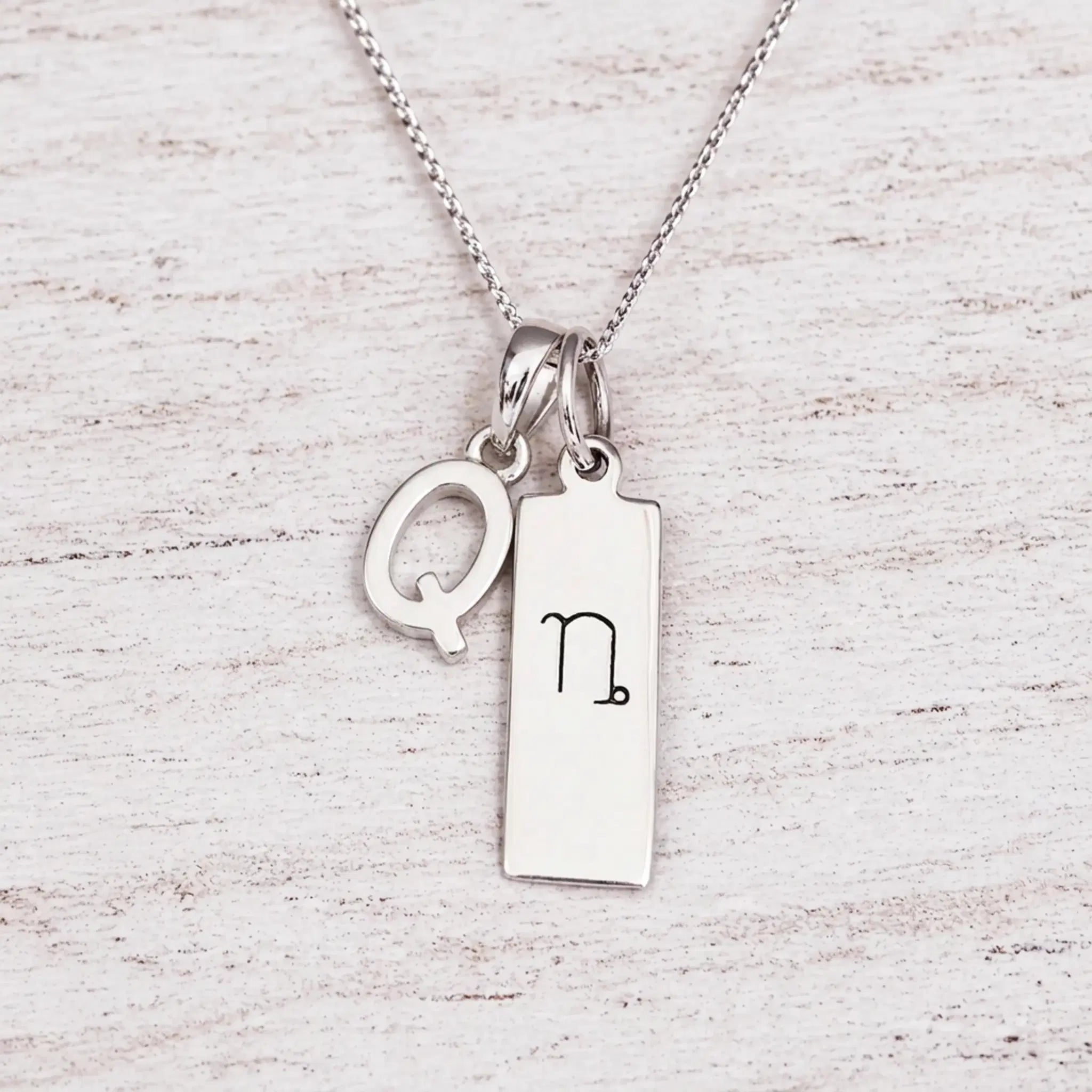 sterling silver initial Q pendant and capricorn necklace on a fine silver chain against a light wooden background