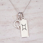 Sterling silver Q initial and GeminI Necklace on a fine silver chain on a light wooden background
