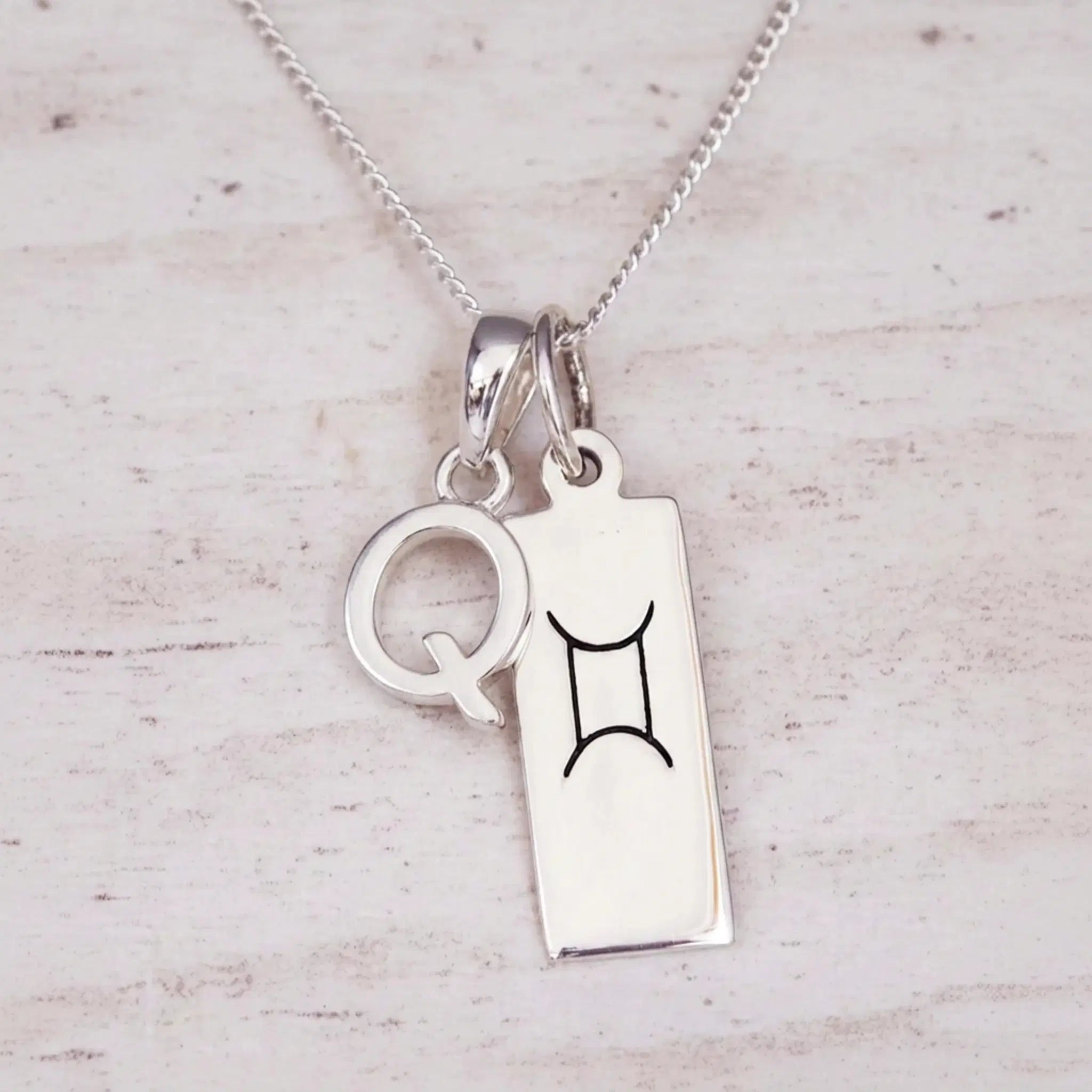 Sterling silver Q initial and GeminI Necklace on a fine silver chain on a light wooden background