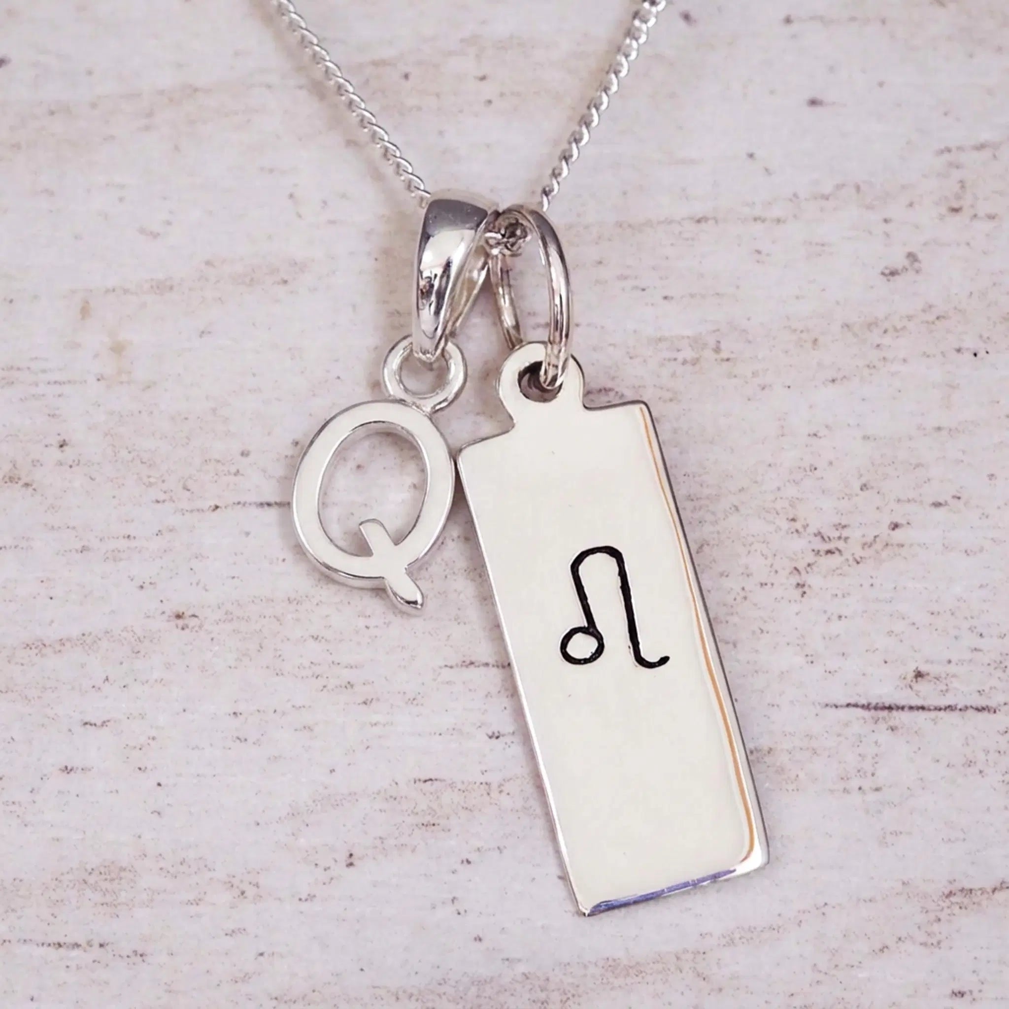 sterling silver initial q leo zodiac star sign pendant necklace against a light wooden background