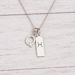 sterling silver Q initial Pisces Necklace on a fine silver chain against a light wooden background