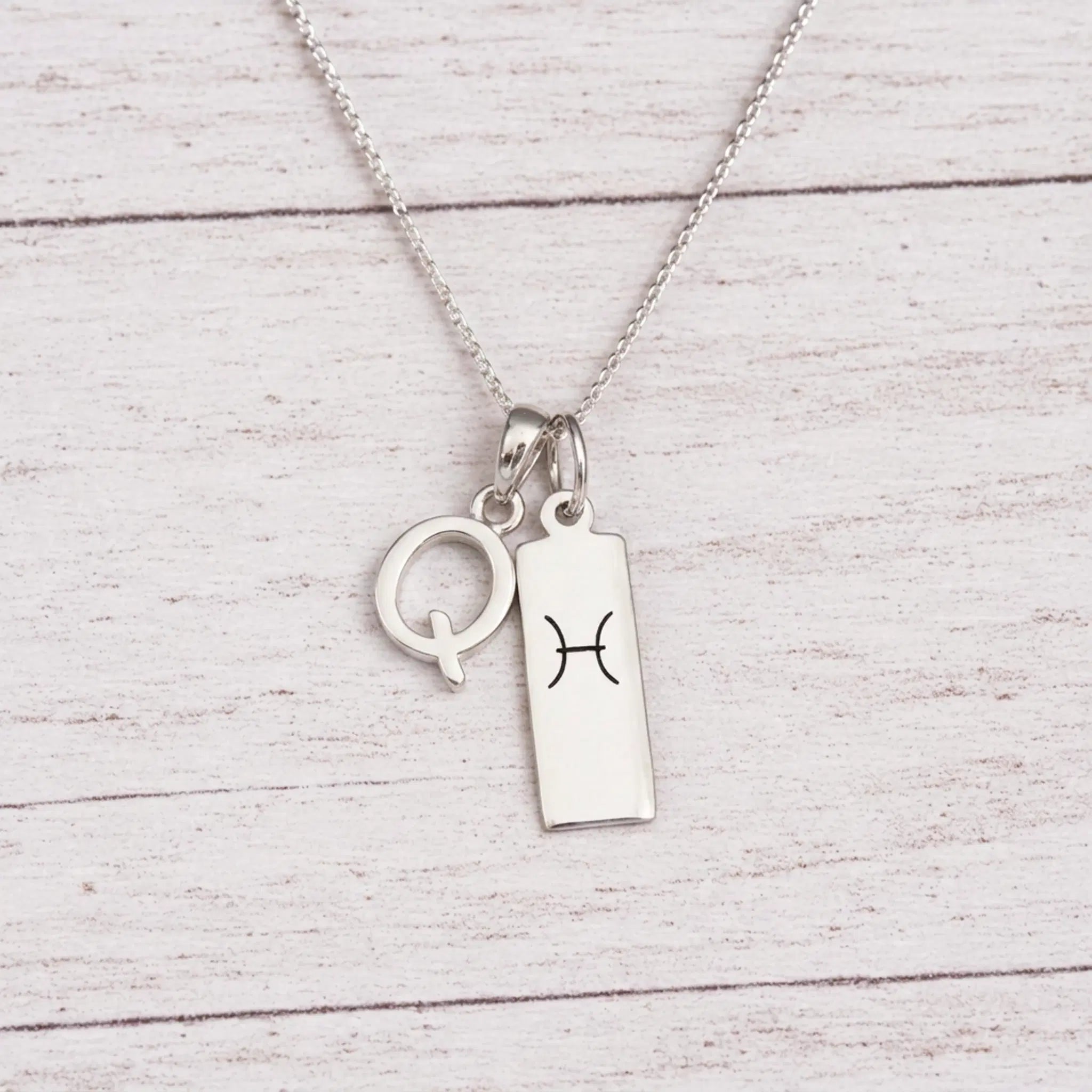 sterling silver Q initial Pisces Necklace on a fine silver chain against a light wooden background