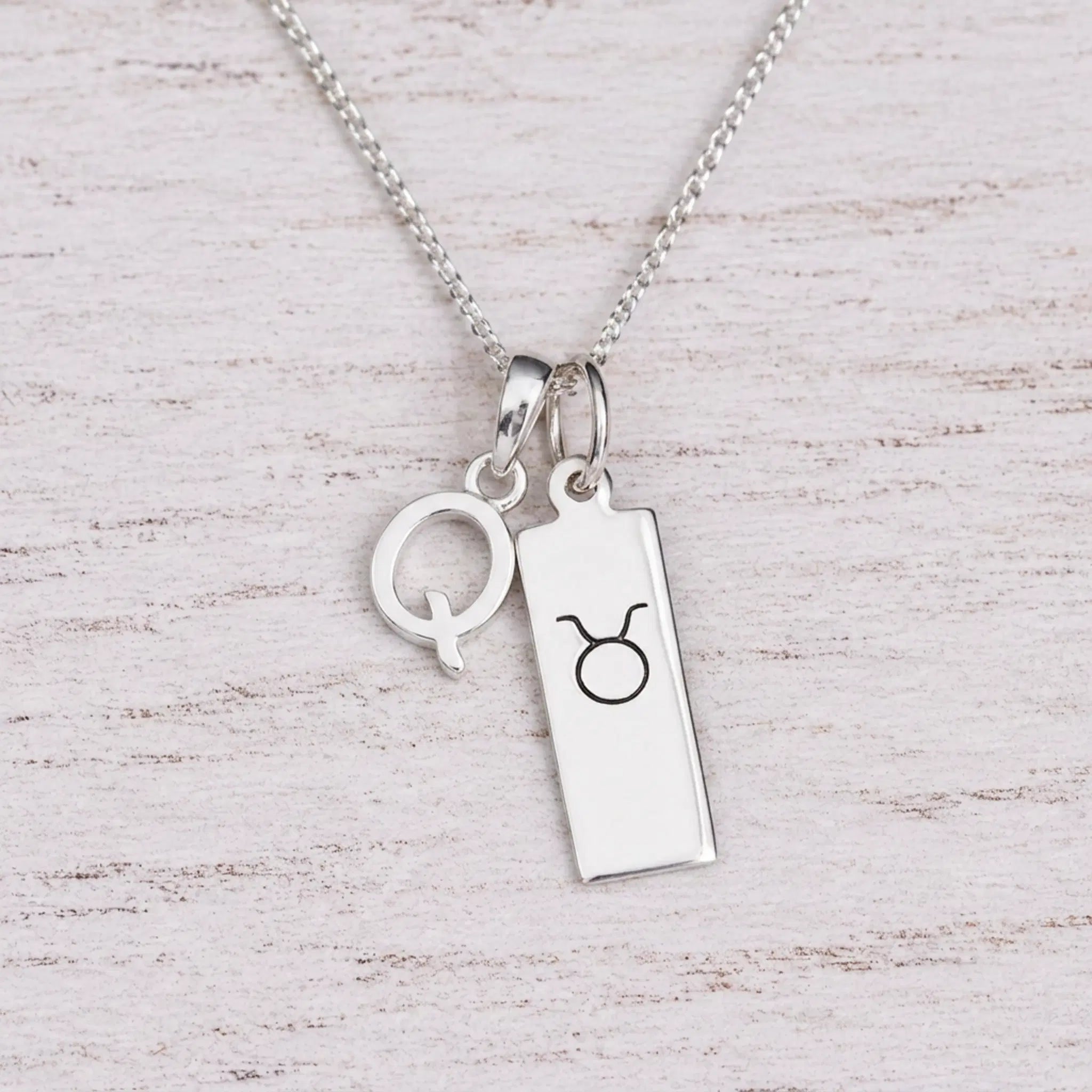 Sterling silver Q initial Pendant and Taurus Necklace on a fine silver chain on a light wooden background