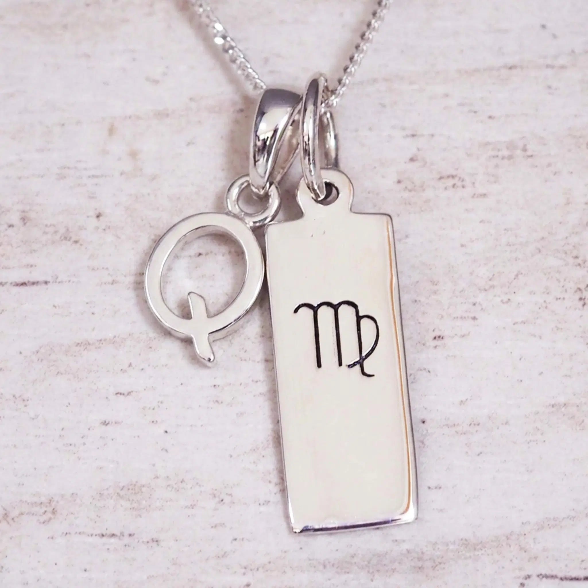 sterling silver initial q virgo zodiac star sign pendant necklace against a light wooden background