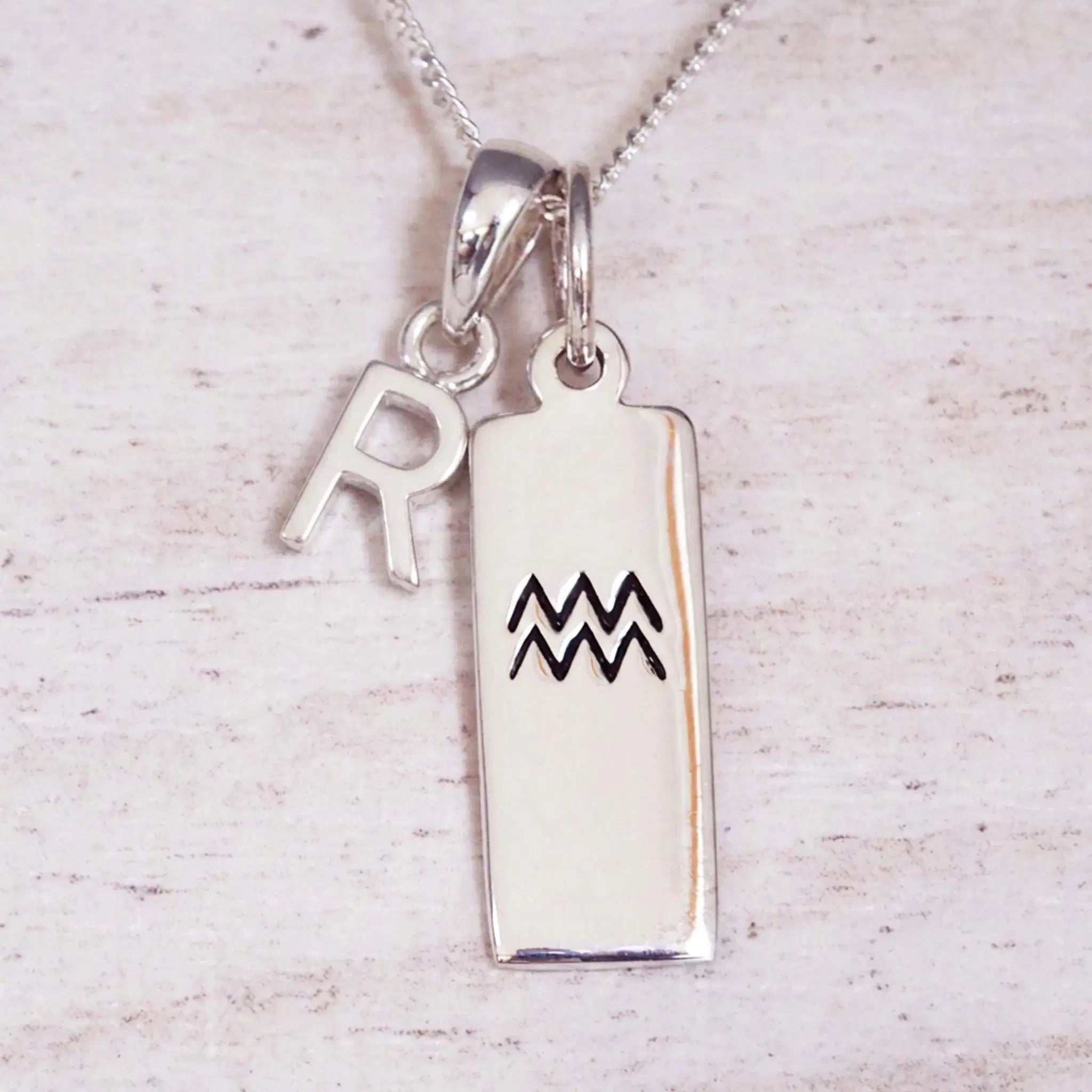 Sterling Silver R Initial and Aquarius Necklace on a fine silver chain against a light wooden background