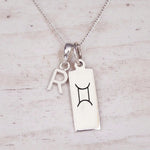 Sterling silver R initial and GeminI Necklace on a fine silver chain on a light wooden background