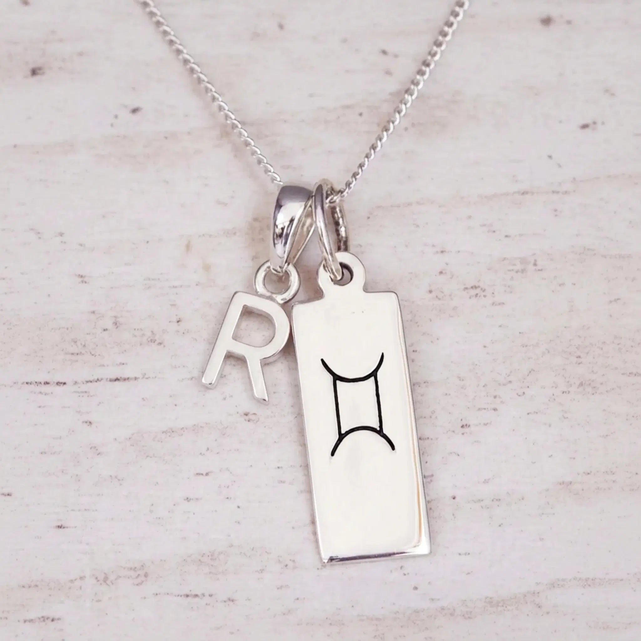 Sterling silver R initial and GeminI Necklace on a fine silver chain on a light wooden background