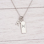 sterling silver R initial Pisces Necklace on a fine silver chain against a light wooden background