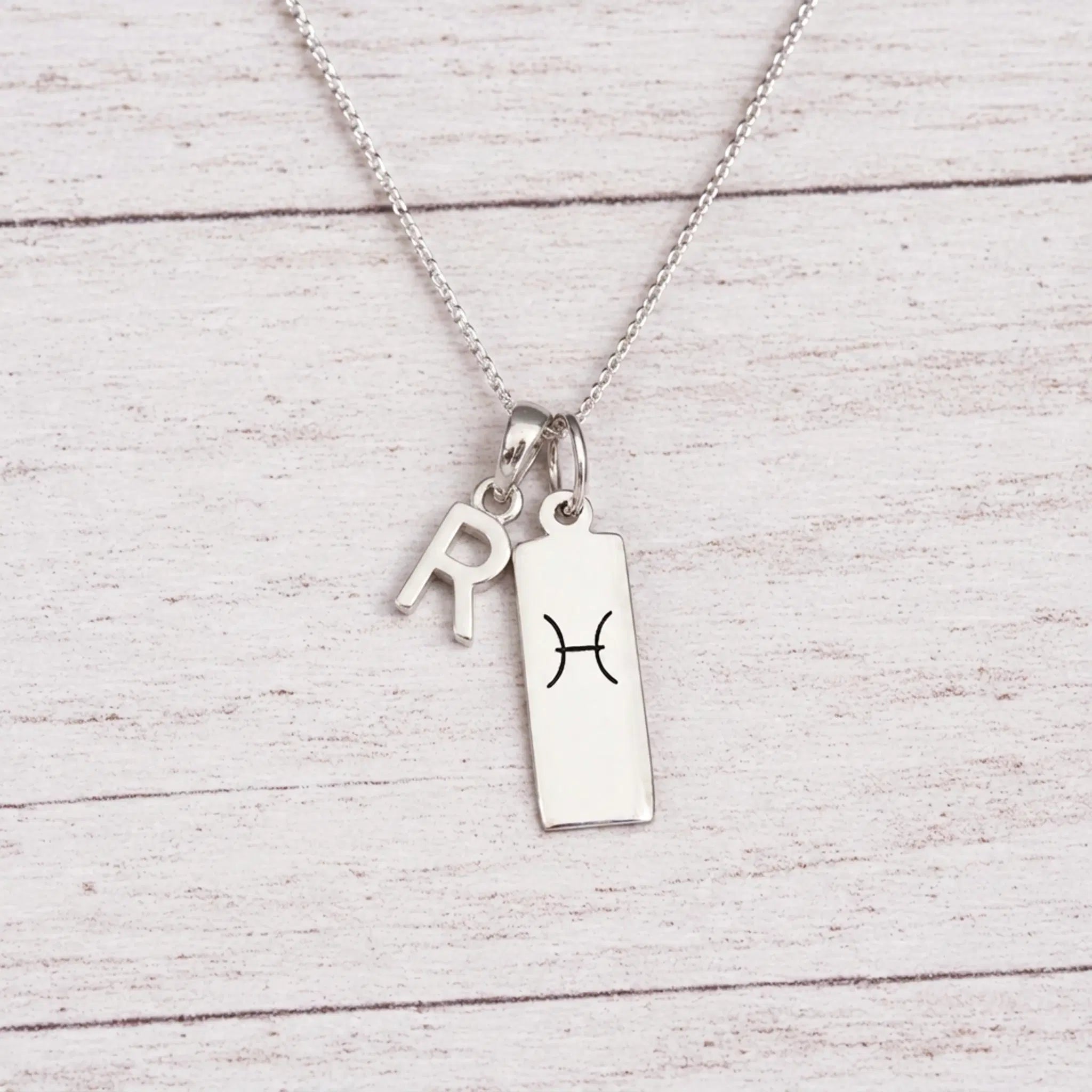 sterling silver R initial Pisces Necklace on a fine silver chain against a light wooden background