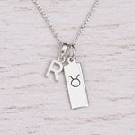 Sterling silver R initial Pendant and Taurus Necklace on a fine silver chain on a light wooden background
