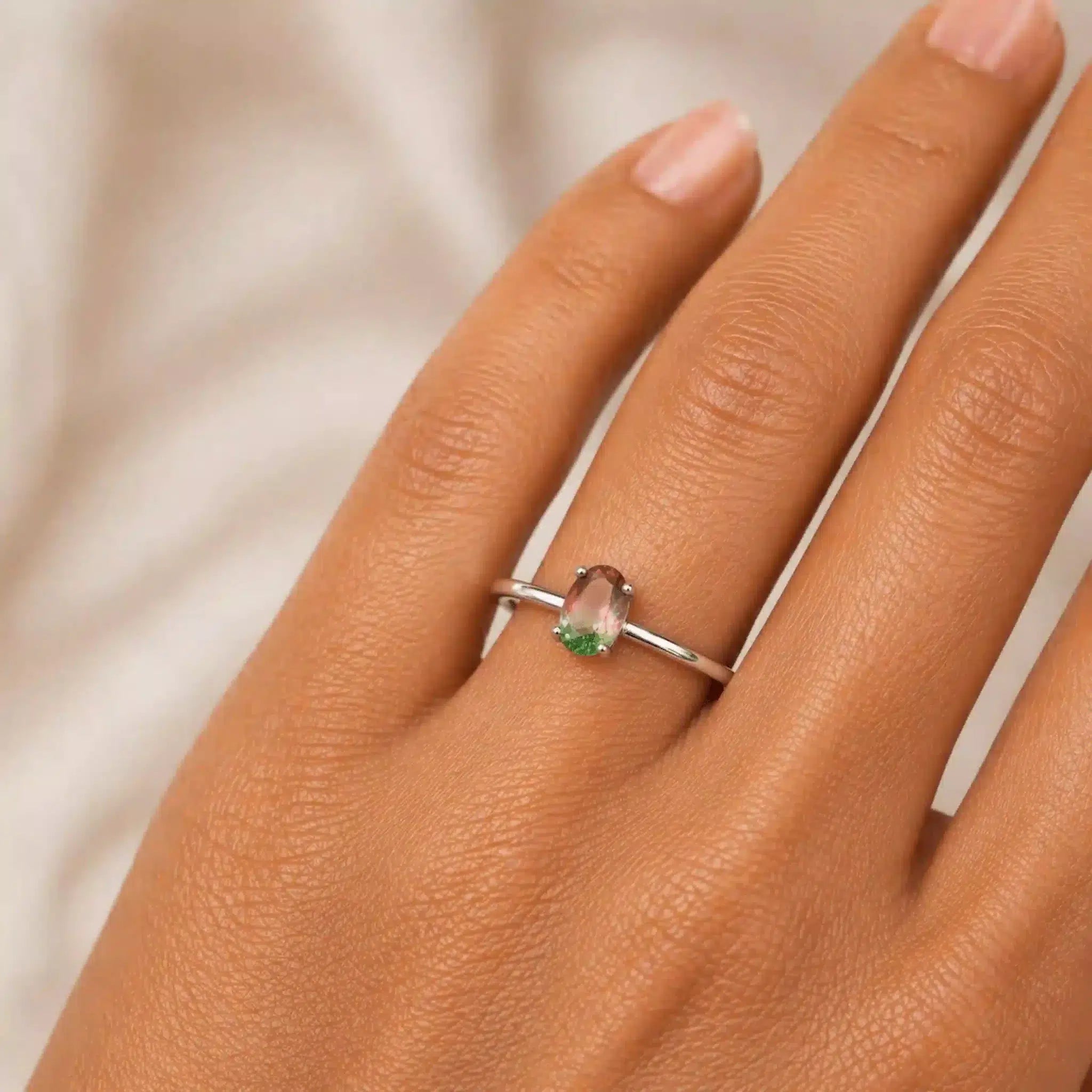 Silver ring with a multicoloured tourmaline gemstone on a hand against a neutral background