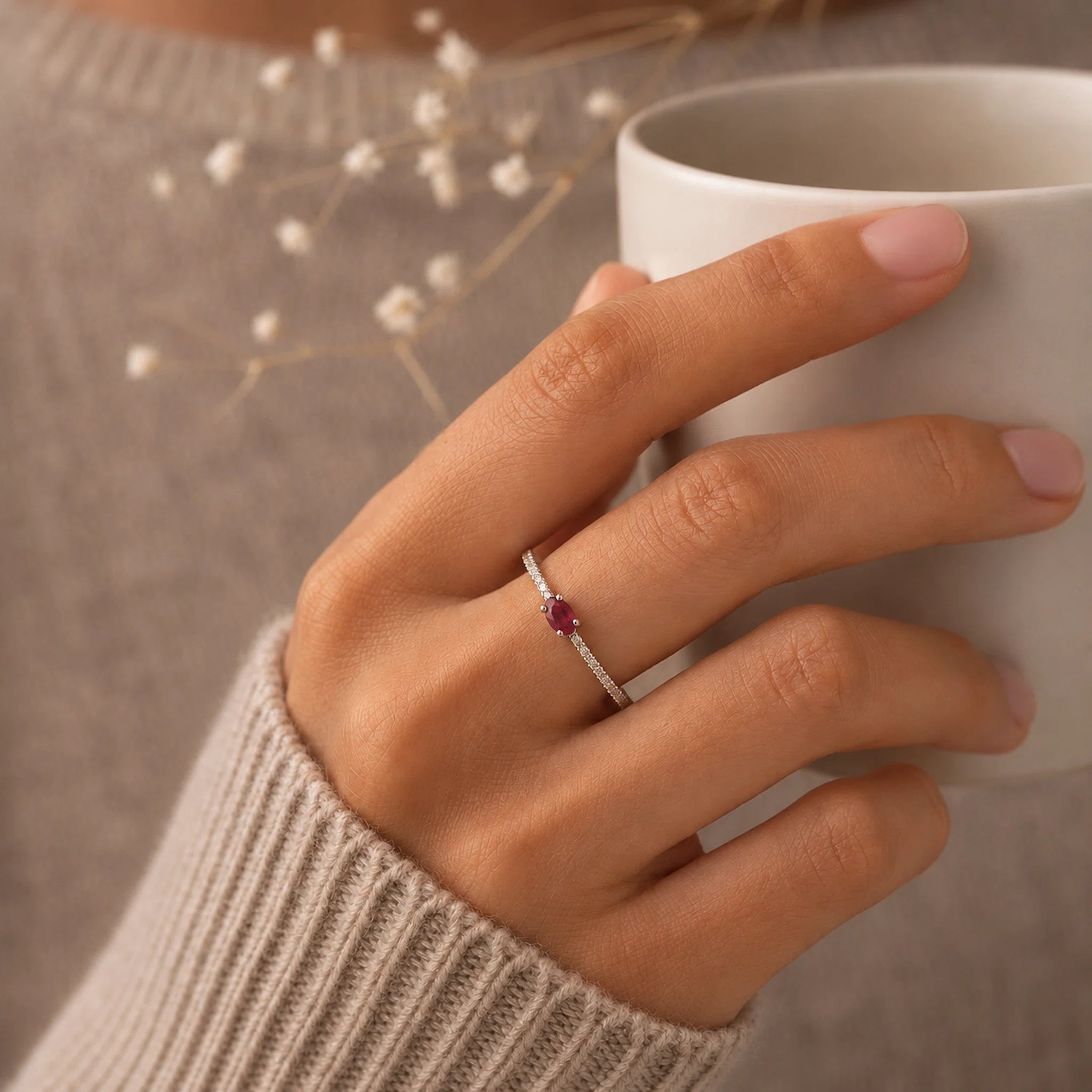 Hand holding a white mug with a sterling silver cubic zirconia pave stacking ring featuring a natural red ruby gemstone