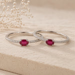 Two sterling silver rings with red ruby gemstones on a beige surface with dried flowers.
