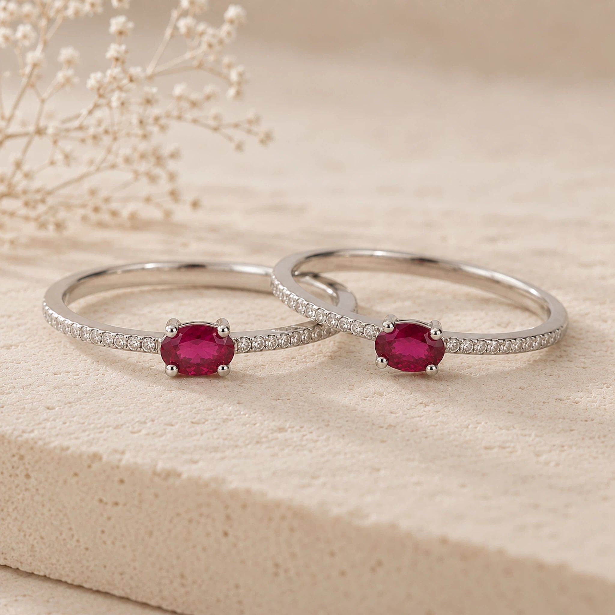 Two sterling silver rings with red ruby gemstones on a beige surface with dried flowers.