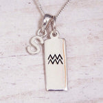 Sterling Silver S Initial and Aquarius Necklace on a fine silver chain against a light wooden background