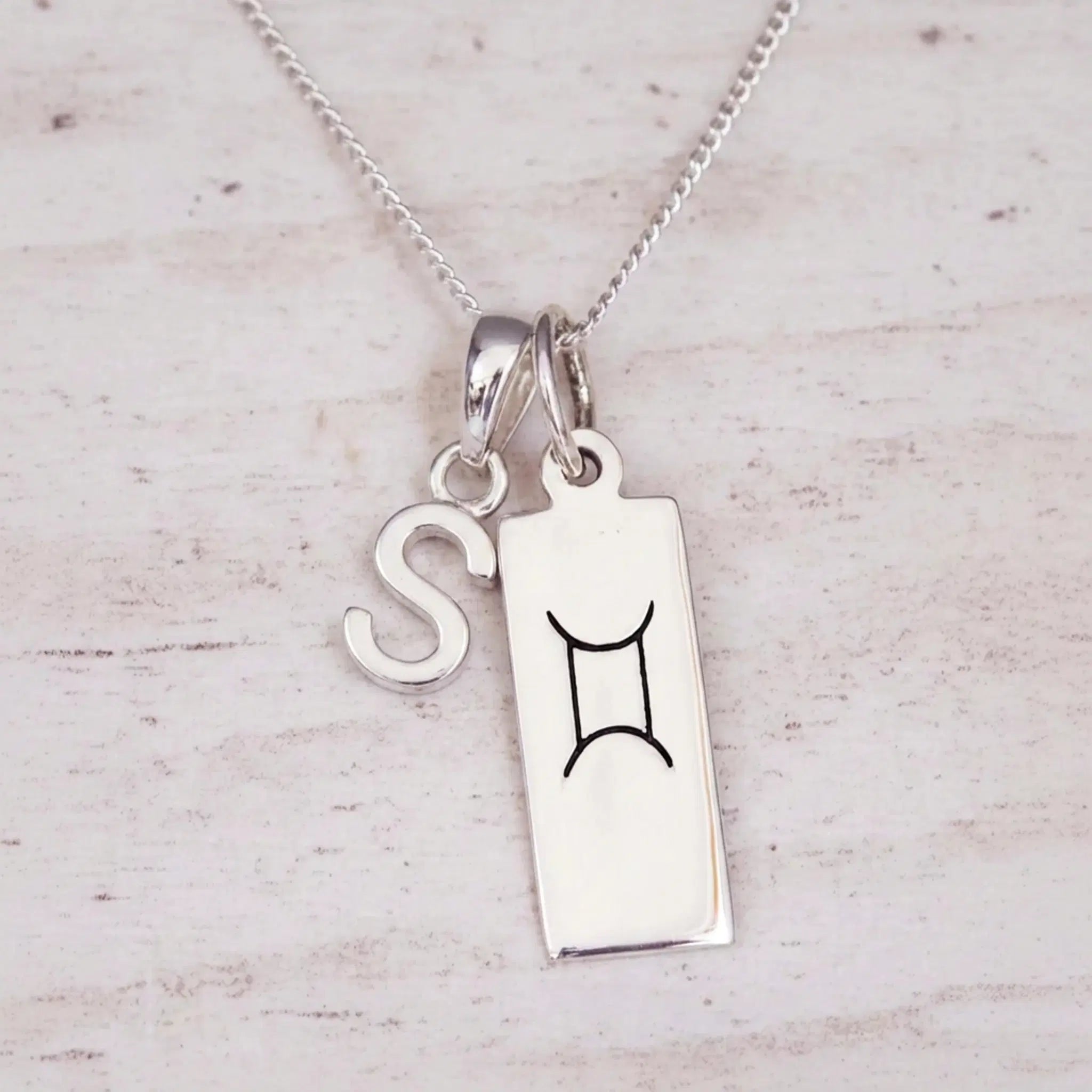 Sterling silver S initial and GeminI Necklace on a fine silver chain on a light wooden background
