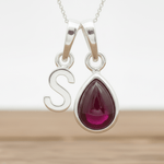 Silver s initial necklace with a teardrop-shaped red ruby gemstone pendant on a white background