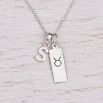 Sterling silver S initial Pendant and Taurus Necklace on a fine silver chain on a light wooden background