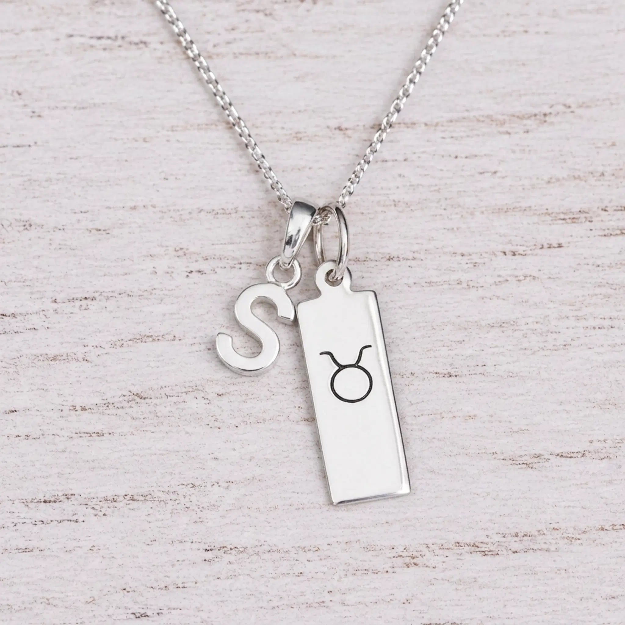 Sterling silver S initial Pendant and Taurus Necklace on a fine silver chain on a light wooden background