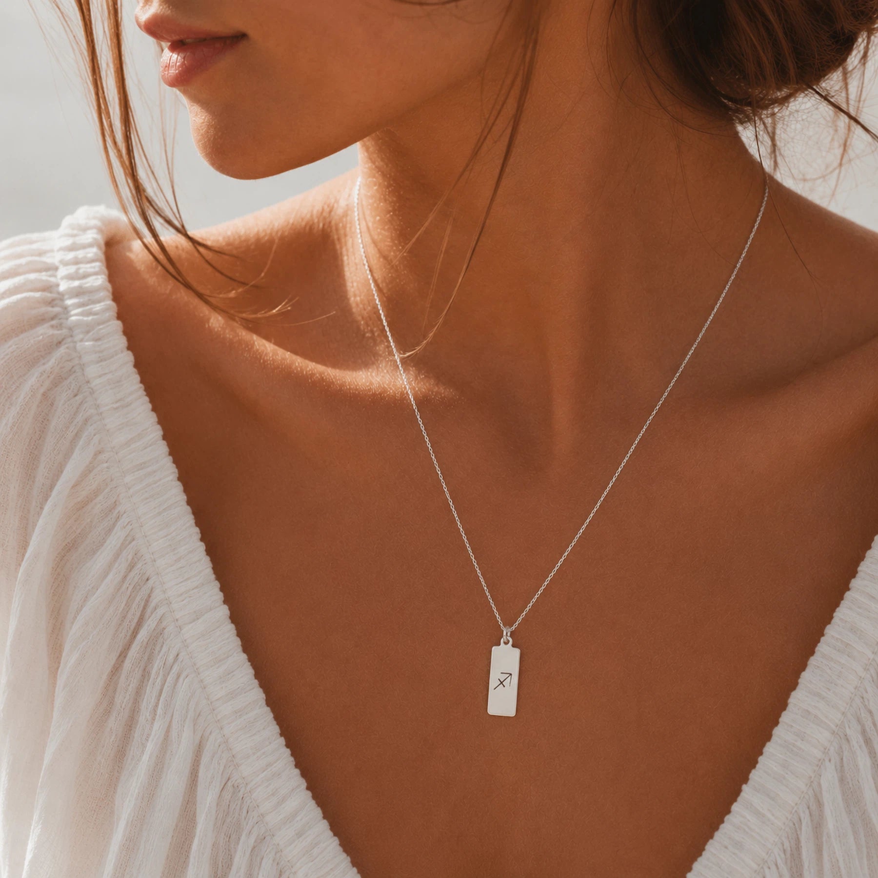 model wearing a dainty sterling silver fine chain necklace with a rectangle pendant engraved with sagittarius zodiac line glyph symbol.