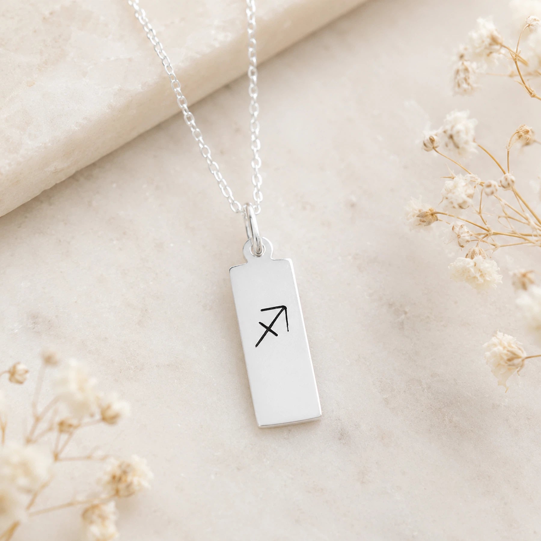 dainty sterling silver fine chain necklace with a rectangle pendant engraved with sagittarius zodiac line glyph symbol.