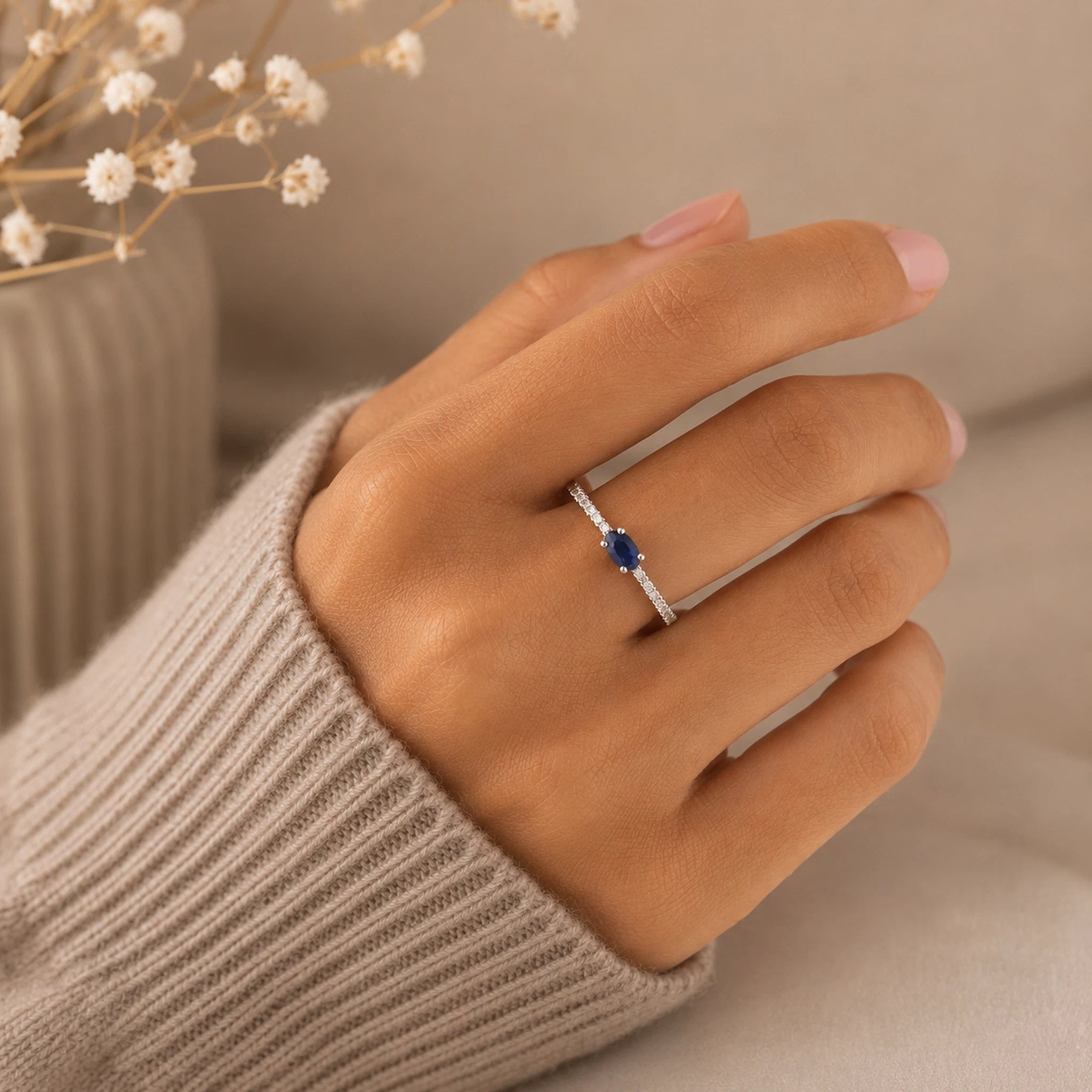 Hand wearing a sterling silver pave style ring with a blue sapphire gemstone on a neutral background