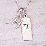 Silver Initial and Scorpio Zodiac Necklace with a letter H pendant and engraved Scorpio bar, flat lay on light wood