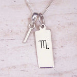 Silver Initial and Scorpio Zodiac Necklace with a letter I pendant and engraved Scorpio bar, flat lay on light wood