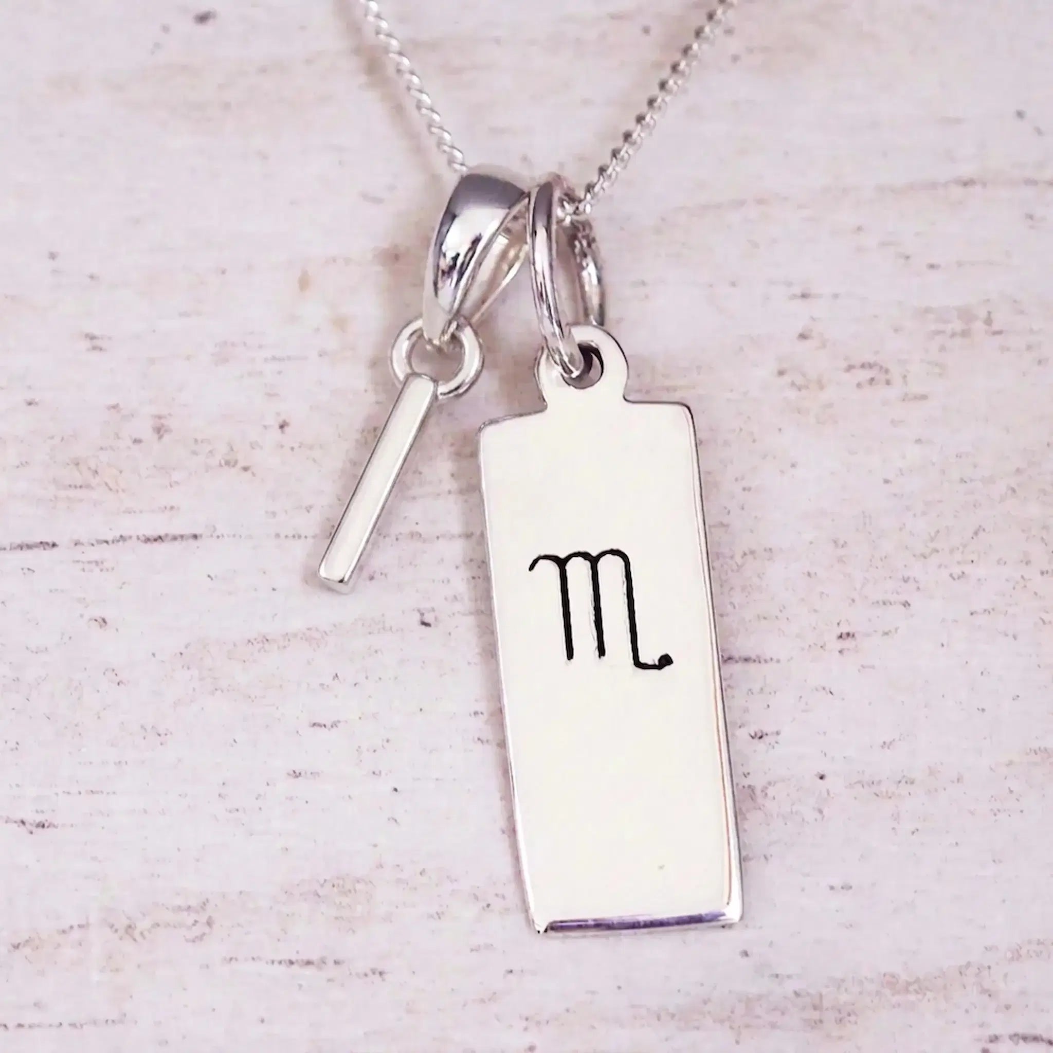 Silver Initial and Scorpio Zodiac Necklace with a letter I pendant and engraved Scorpio bar, flat lay on light wood