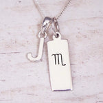 Silver Initial and Scorpio Zodiac Necklace with a letter J pendant and engraved Scorpio bar, flat lay on light wood