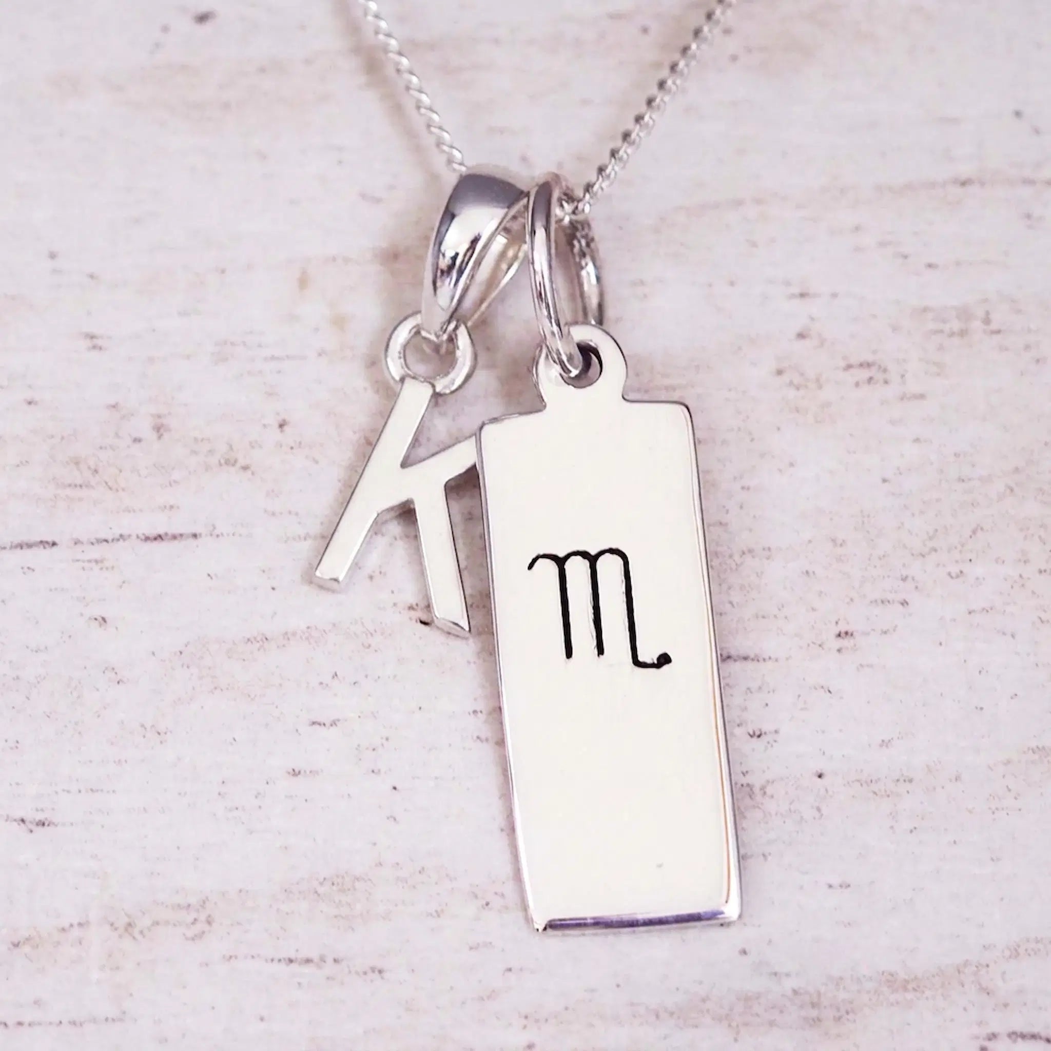 Silver Initial and Scorpio Zodiac Necklace with a letter K pendant and engraved Scorpio bar, flat lay on light wood