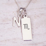 Silver Initial and Scorpio Zodiac Necklace with a letter N pendant and engraved Scorpio bar, flat lay on light wood