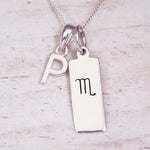 Silver Initial and Scorpio Zodiac Necklace with a letter P pendant and engraved Scorpio bar, flat lay on light wood
