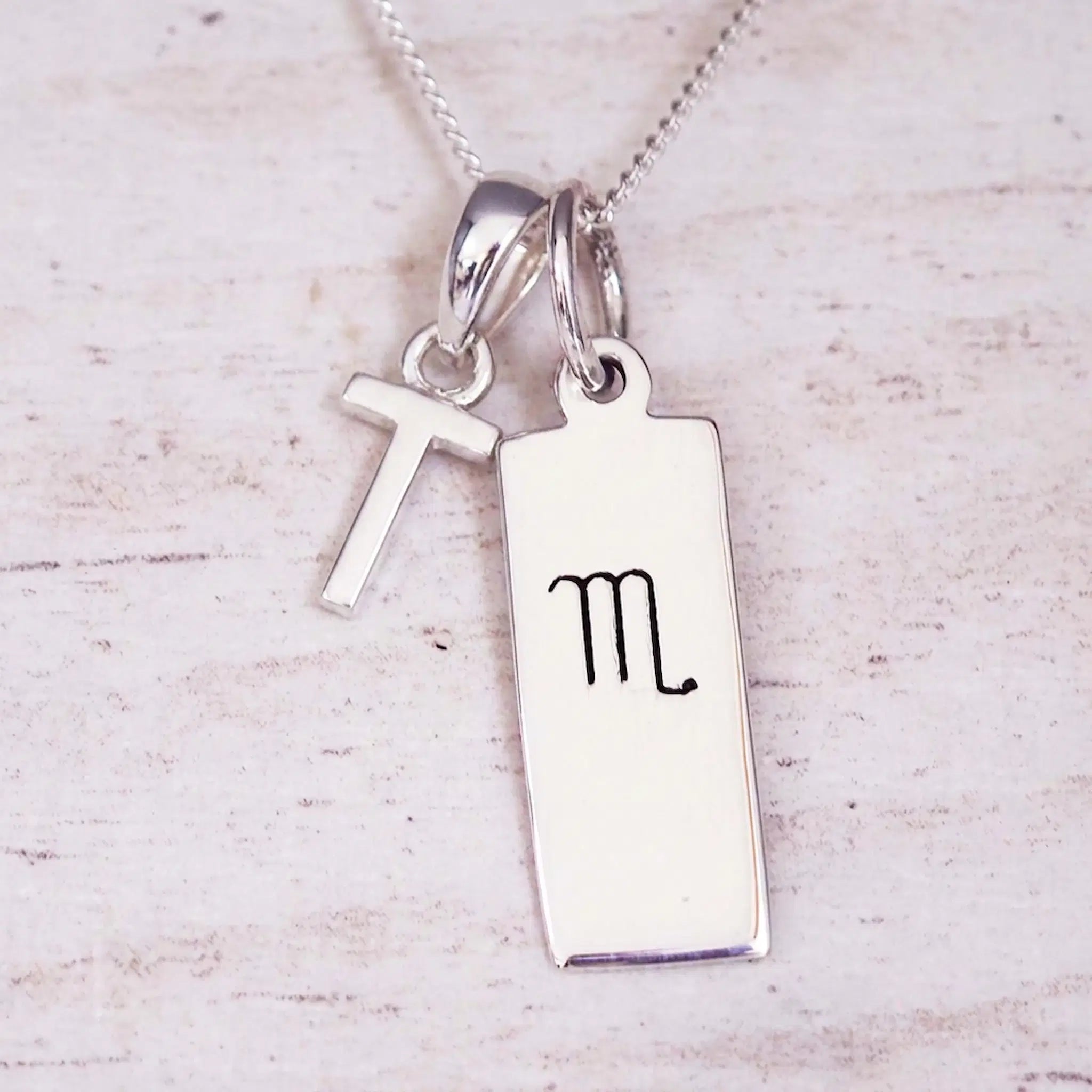 Silver Initial and Scorpio Zodiac Necklace with a letter T pendant and engraved Scorpio bar, flat lay on light wood