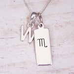 Silver Initial and Scorpio Zodiac Necklace with a letter W pendant and engraved Scorpio bar, flat lay on light wood