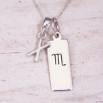 Silver Initial and Scorpio Zodiac Necklace with a letter X pendant and engraved Scorpio bar, flat lay on light wood