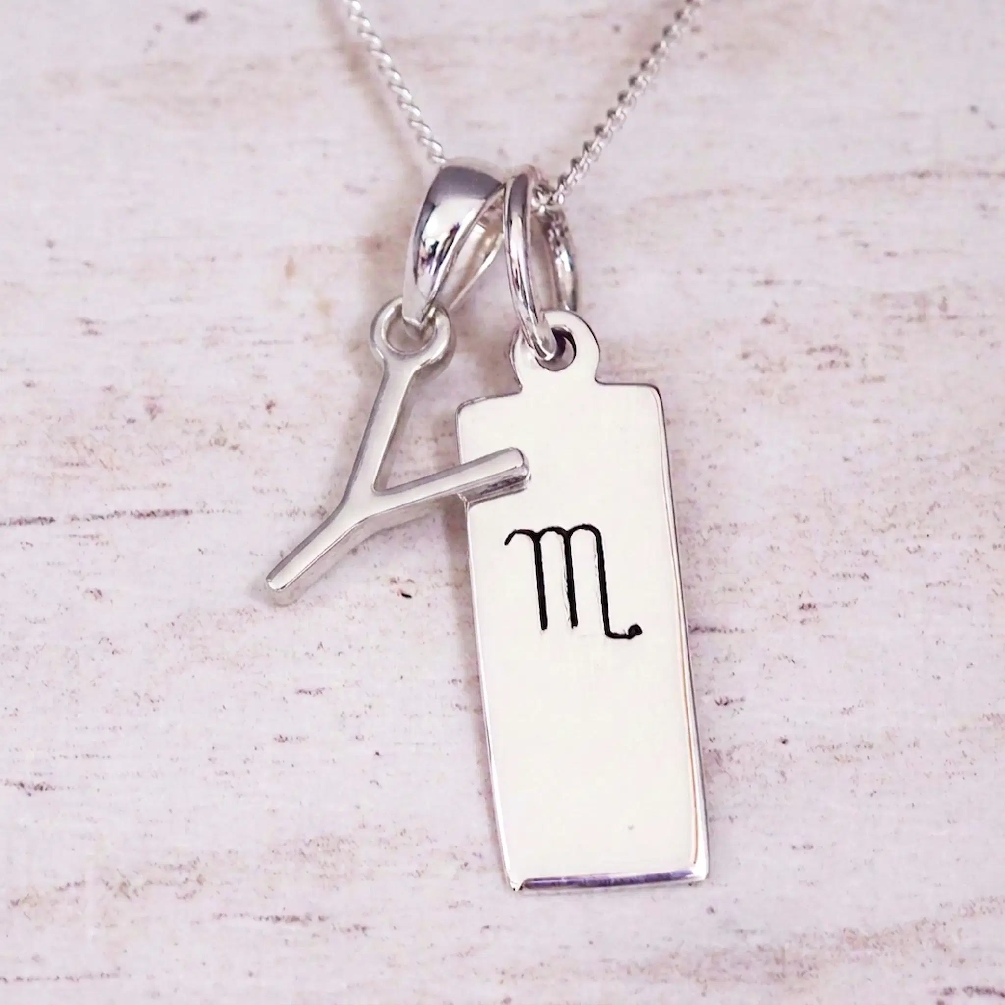 Silver Initial and Scorpio Zodiac Necklace with a letter Y pendant and engraved Scorpio bar, flat lay on light wood