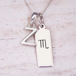 Silver Initial and Scorpio Zodiac Necklace with a letter Z pendant and engraved Scorpio bar, flat lay on light wood