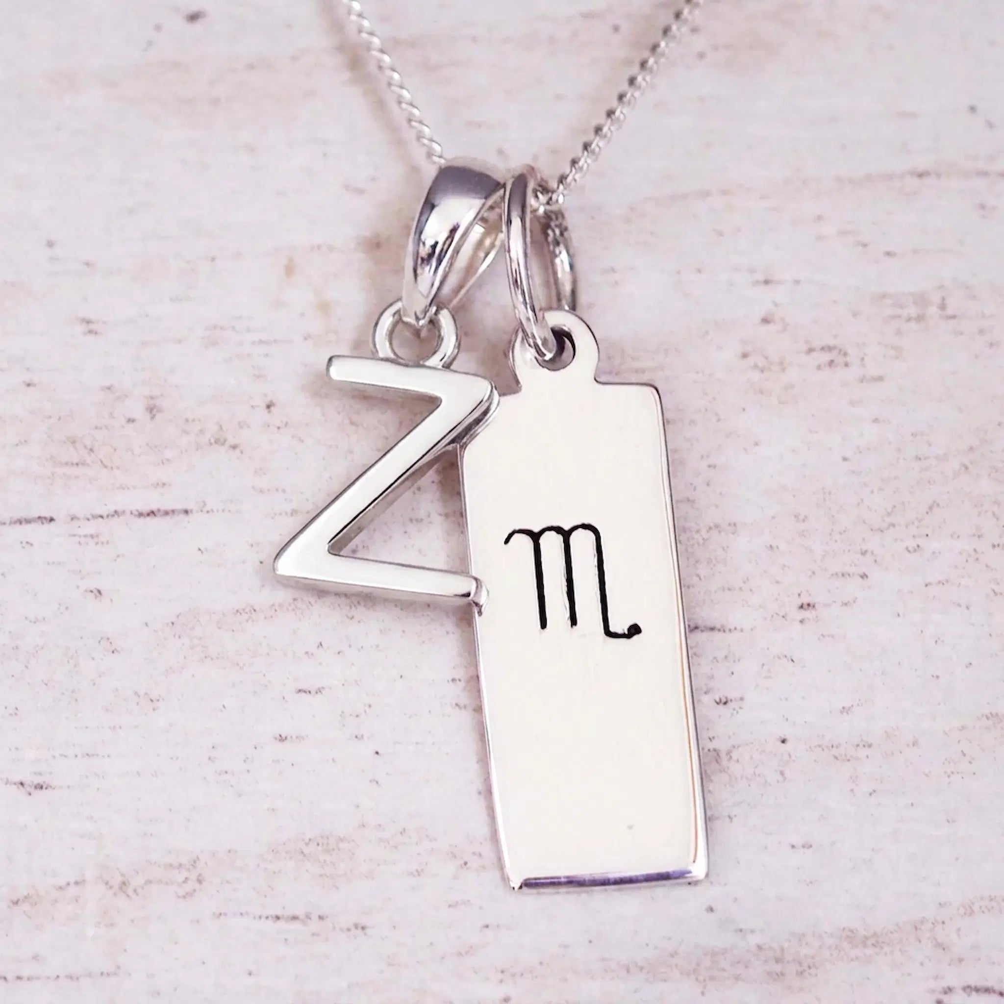 Silver Initial and Scorpio Zodiac Necklace with a letter Z pendant and engraved Scorpio bar, flat lay on light wood