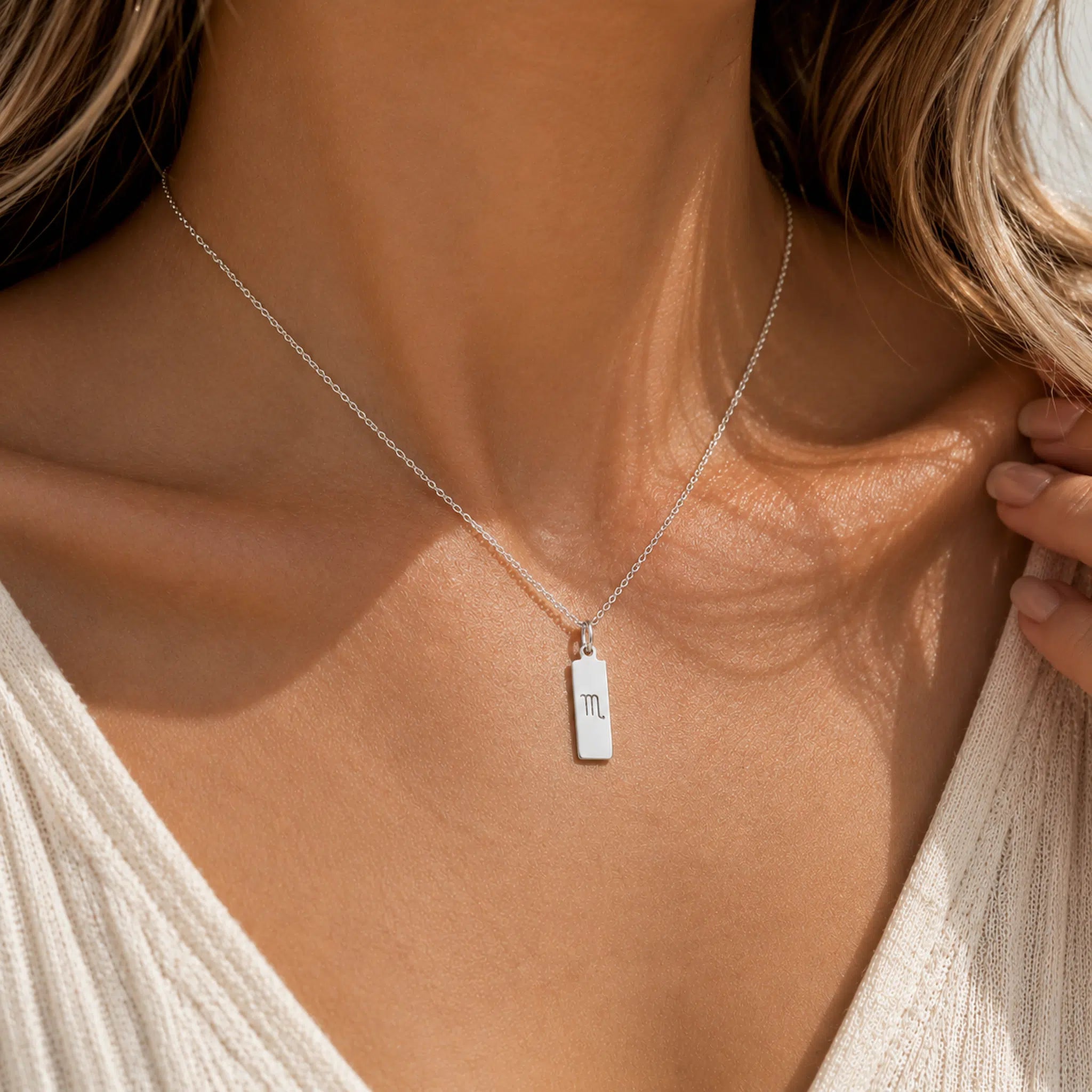 close up of a woman wearing a sterling silver scorpio necklace with rectangle pendant featuring engraved minimalist scorpio zodiac star sign line glyph symbol suspended from a fine chain