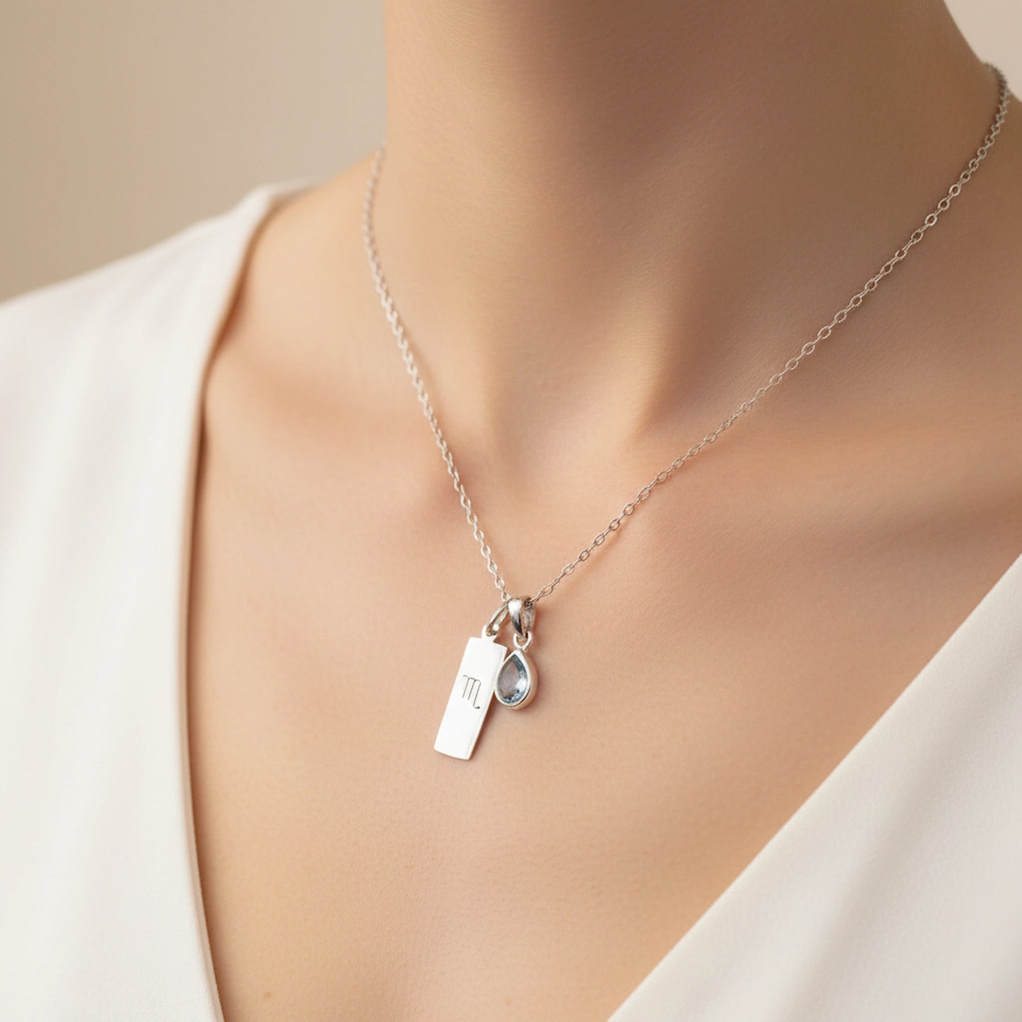 woman wearing a sterling silver necklace with scorpio zodiac pendant and a November birthstone topaz pendant