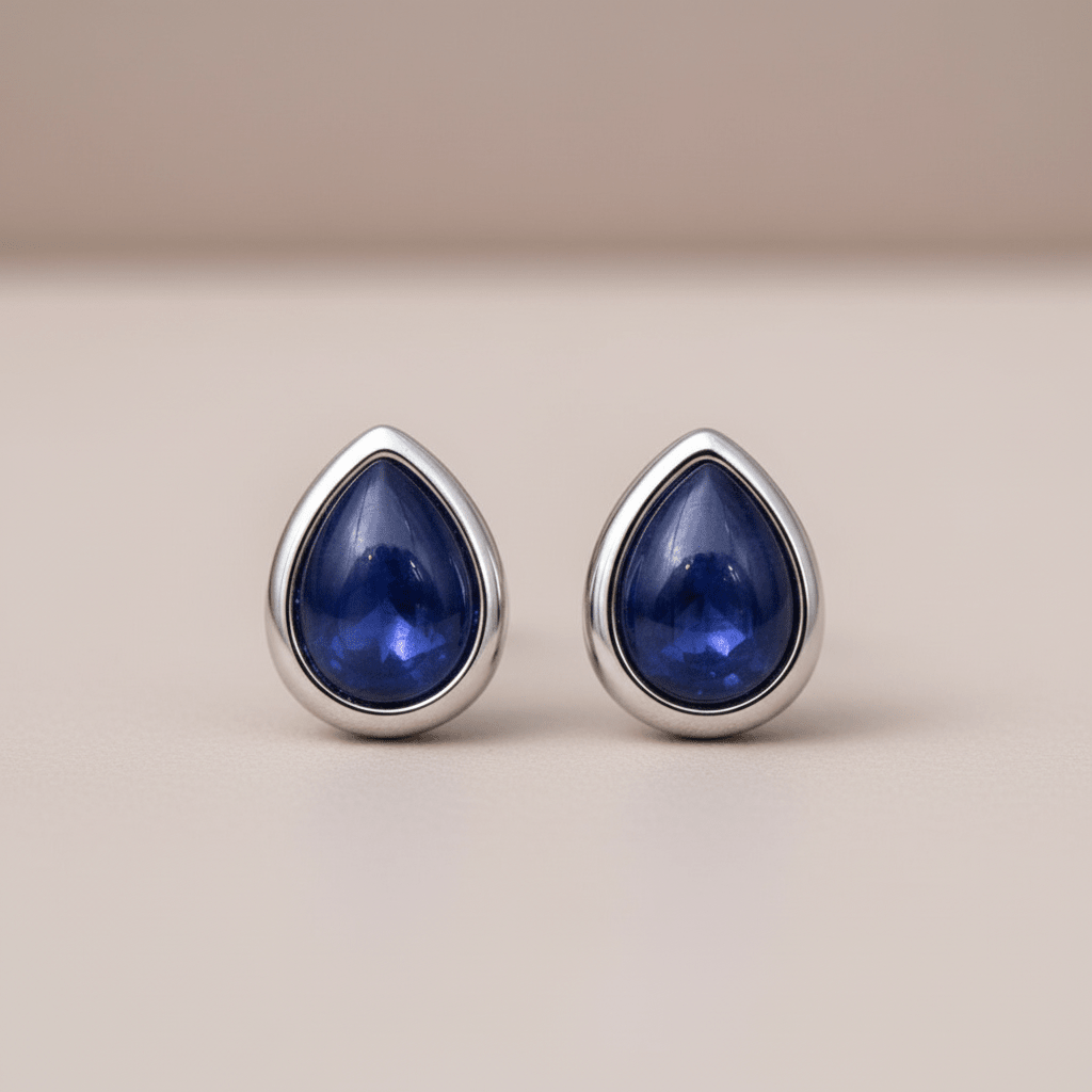 Teardrop-shaped blue gemstone earrings with silver settings on a beige background