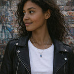 woman with black hair and leather jacket wearing a silver necklace with dark blue crystal pendant