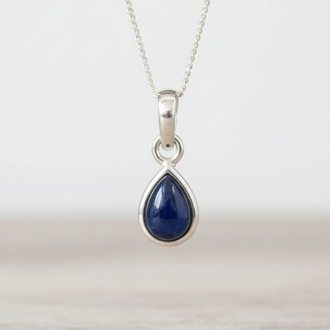 Teardrop-shaped blue sapphire pendant on a silver chain against a white background