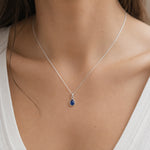 close up of model wearing a dainty sterling silver september birthstone natural sapphire teardrop pendant necklace