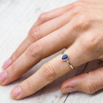 Hand wearing a sterling silver ring with a blue natural sapphire gemstone on a light wooden surface